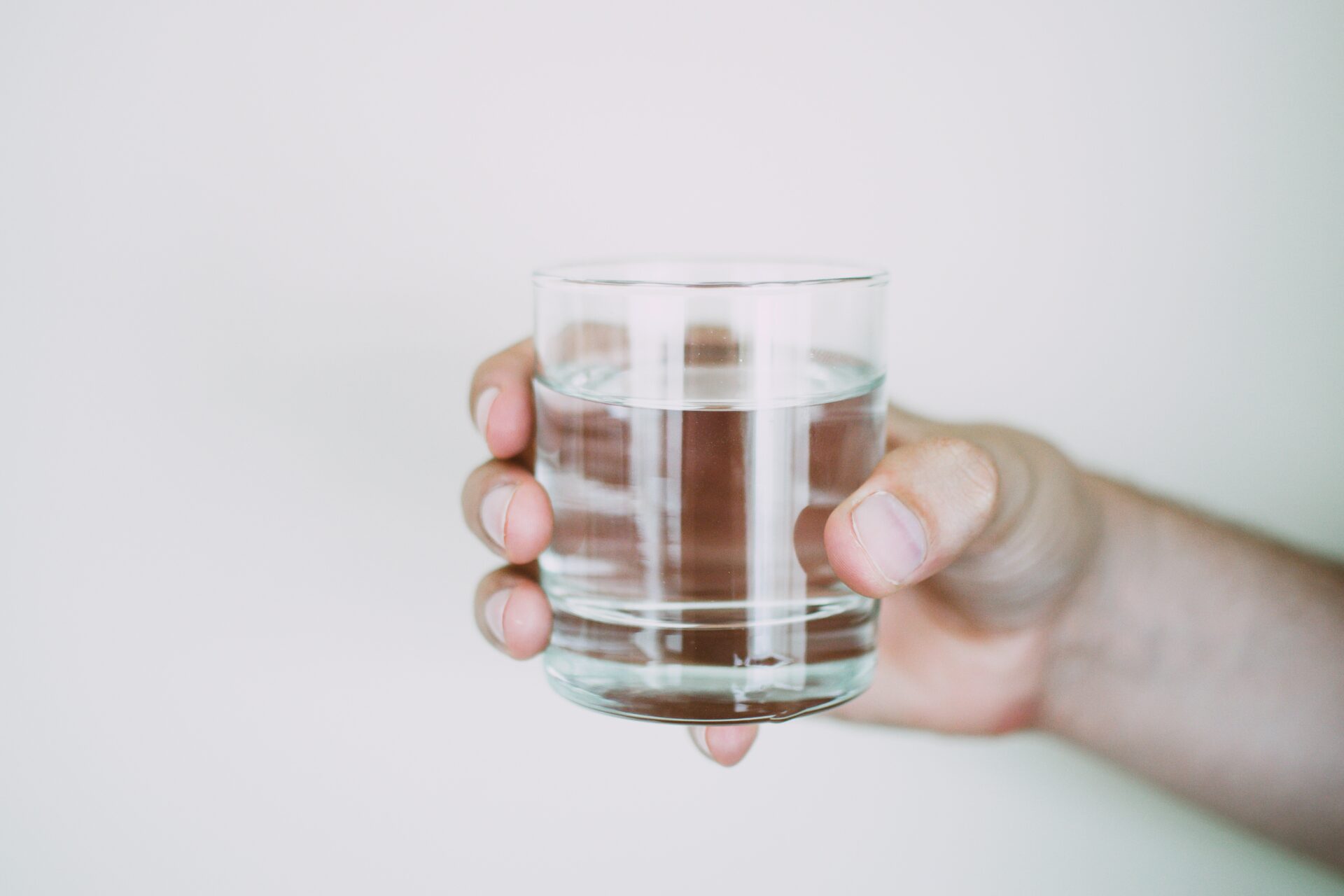 En hand som håller i ett glas med dricksvatten.